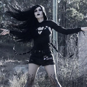 Hexing shrug worn with arms extended outdoors, showing the cropped shoulder layer and hanging straps over a separate fitted outfit.