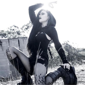 Black hooded crop shrug worn seated outdoors over a separate dark outfit, with lace-up forearms and long hanging straps.