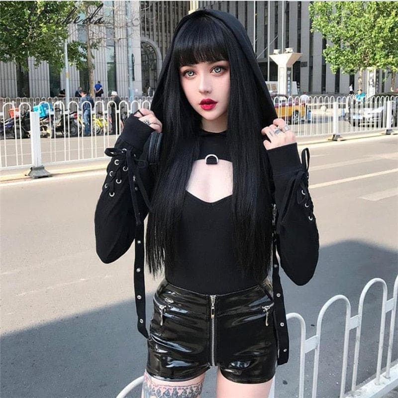 Black hooded crop shrug worn over a separate black top and glossy shorts on a street, with sleeve lacing visible.