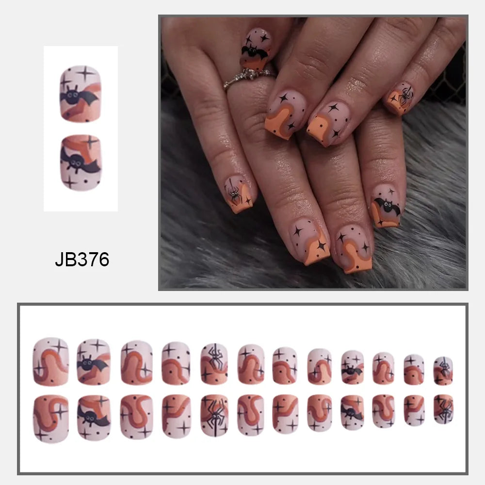 Muted pink square Halloween nails with black bats, orange ghosts and small dark details, shown worn and arranged in rows.