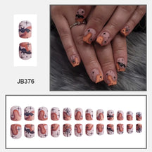 Muted pink square Halloween nails with black bats, orange ghosts and small dark details, shown worn and arranged in rows.