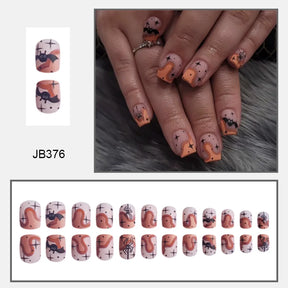 Muted pink square Halloween nails with black bats, orange ghosts and small dark details, shown worn and arranged in rows.