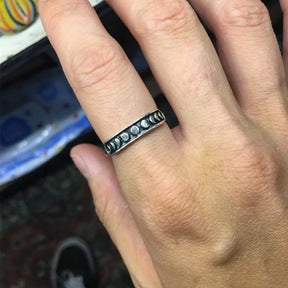 Silver-tone moon phase band worn on a finger, showing the contrasting row of small lunar shapes across its dark front.