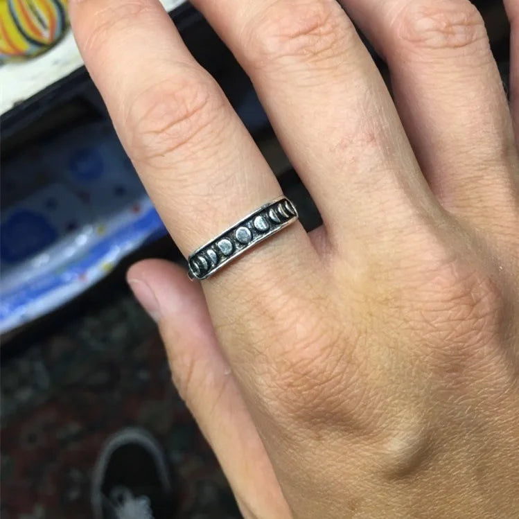 Silver-tone moon phase band worn on a finger, showing the contrasting row of small lunar shapes across its dark front.