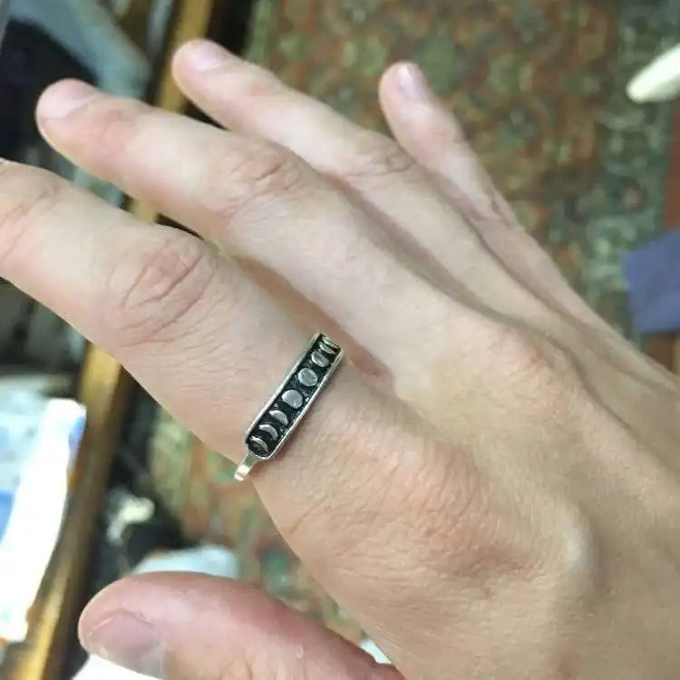 Moon phase ring worn on a hand in natural light, with the dark lunar panel visible above the smooth silver-tone band.