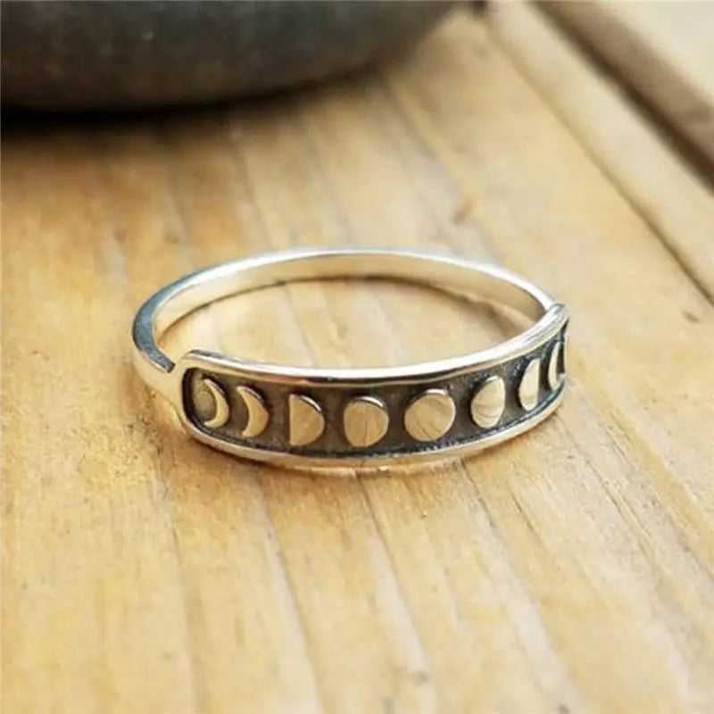 Silver-tone moon phase ring on pale wood, showing the raised crescents and fuller moons across the dark front panel.