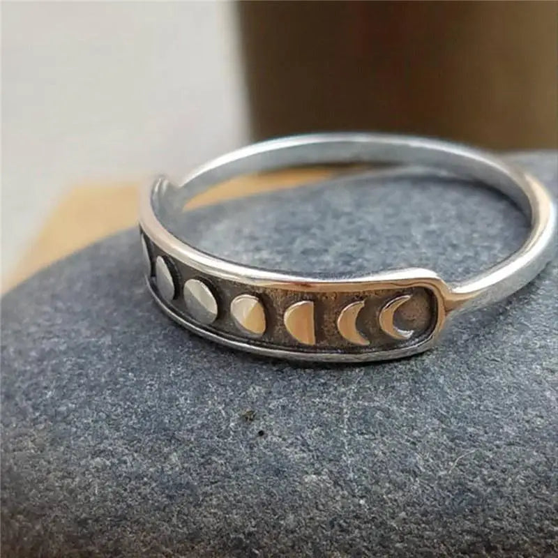 Moon phase ring angled on gray fabric, revealing the smooth narrow rear band and the dark recessed lunar panel at the front.