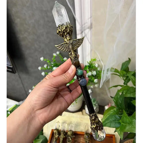 Ornate crystal ritual wand held in a hand, showing its pointed tip, winged ornament and clear sphere end