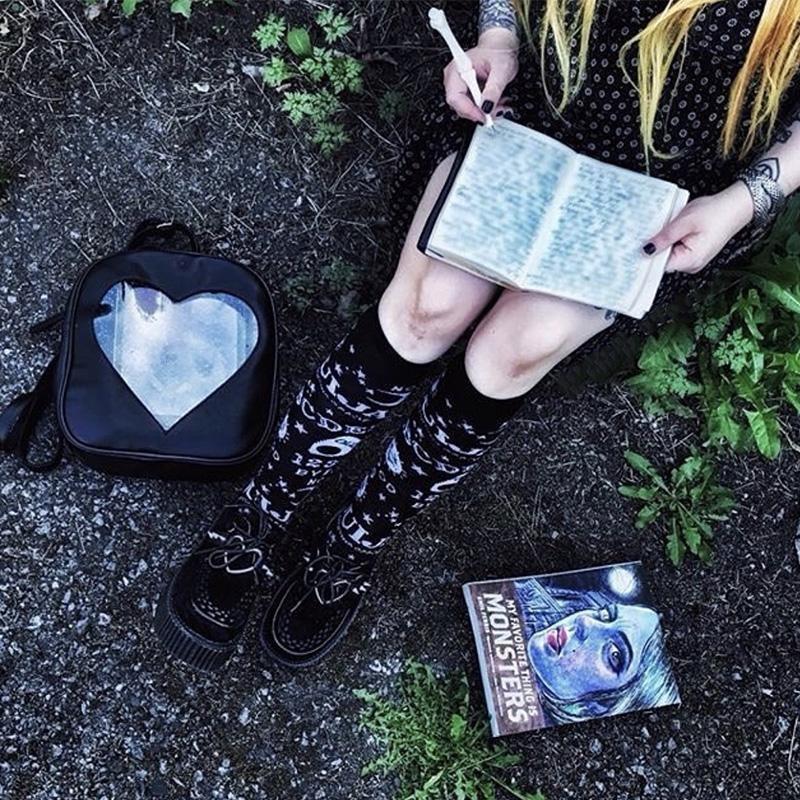Overhead outdoor view of the Ouija knee stockings with black shoes, an open book and a heart-window bag arranged nearby.
