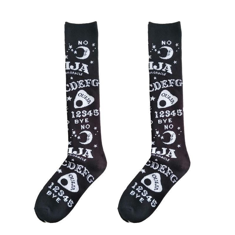Matching black Ouija stockings laid flat side by side on white, with alphabet rows, planchettes and stars continuing down to the feet.