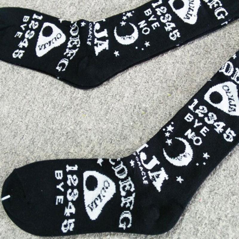 Black Ouija stockings laid flat on pale carpet, showing the spirit-board letters and numbers continuing along the legs and feet.