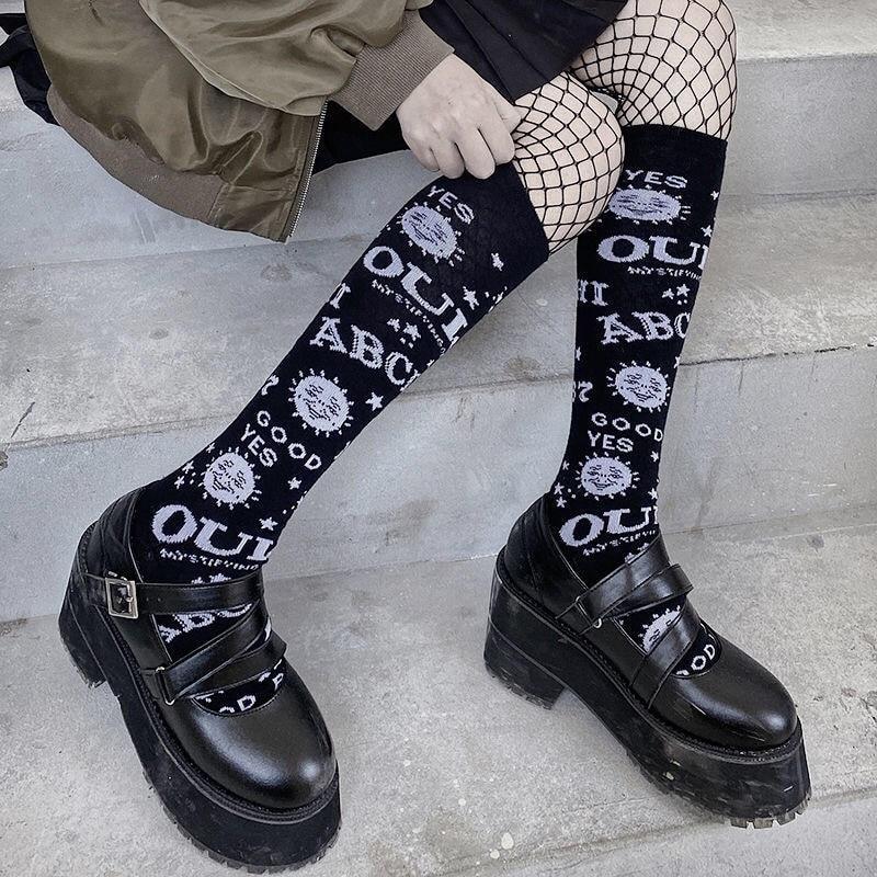 Close styled view of black Ouija knee stockings above chunky buckle shoes, with fishnet tights visible around the knees.