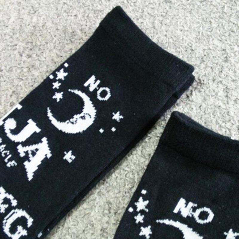 Close-up of a black stocking cuff with a white crescent moon, the word No, small stars and part of the Ouija lettering.