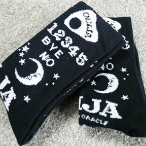 Close view of folded black Ouija stockings, highlighting the crescent moon, white stars, number rows and planchette print.