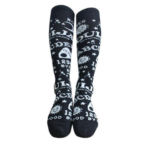 Black Ouija knee stockings worn on two extended legs against a white background, showing the all-around lettering and celestial pattern.
