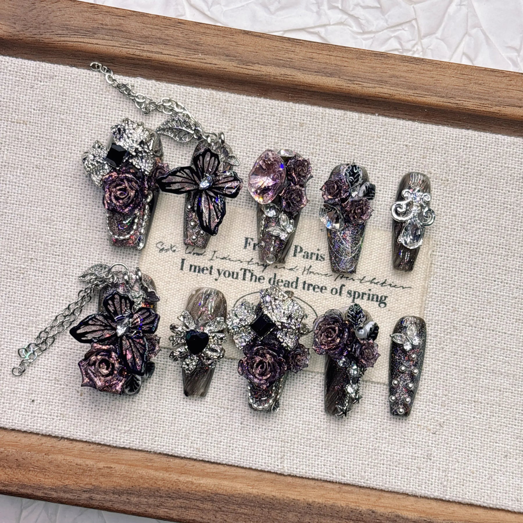 Close view of dark fairy nail art with large black-purple butterfly wings, tiny roses and silver-tone chains on glitter-effect nail bases.