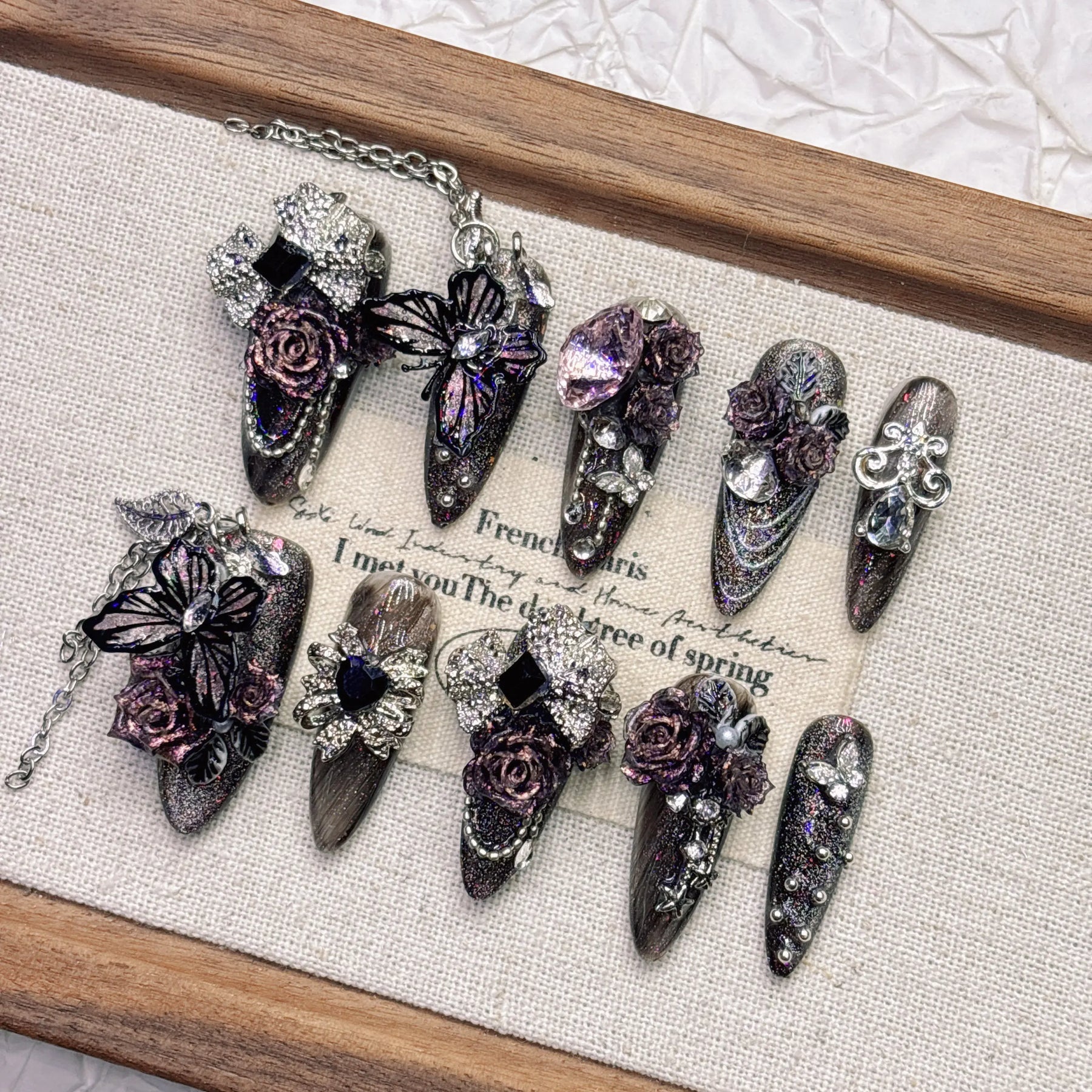 Angled arrangement of black-purple rose and butterfly nails, highlighting purple faceted accents, silver-tone ornament and glittering surfaces.