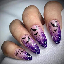 Pink-to-purple pointed Halloween nails worn on a hand, with black bats, white stars and a glittery night-sky effect.