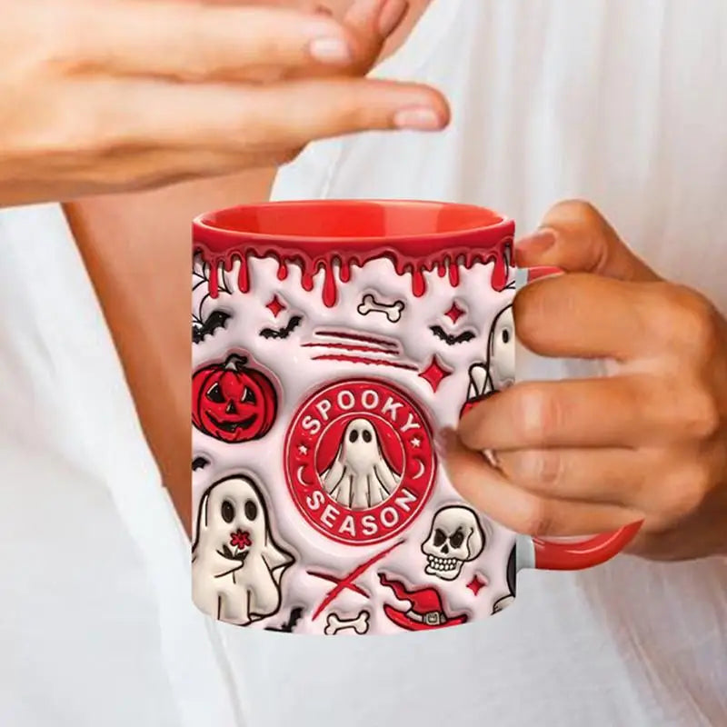 Red-handled Halloween mug held in two hands, showing Spooky Season lettering surrounded by ghosts, bones and skull details.