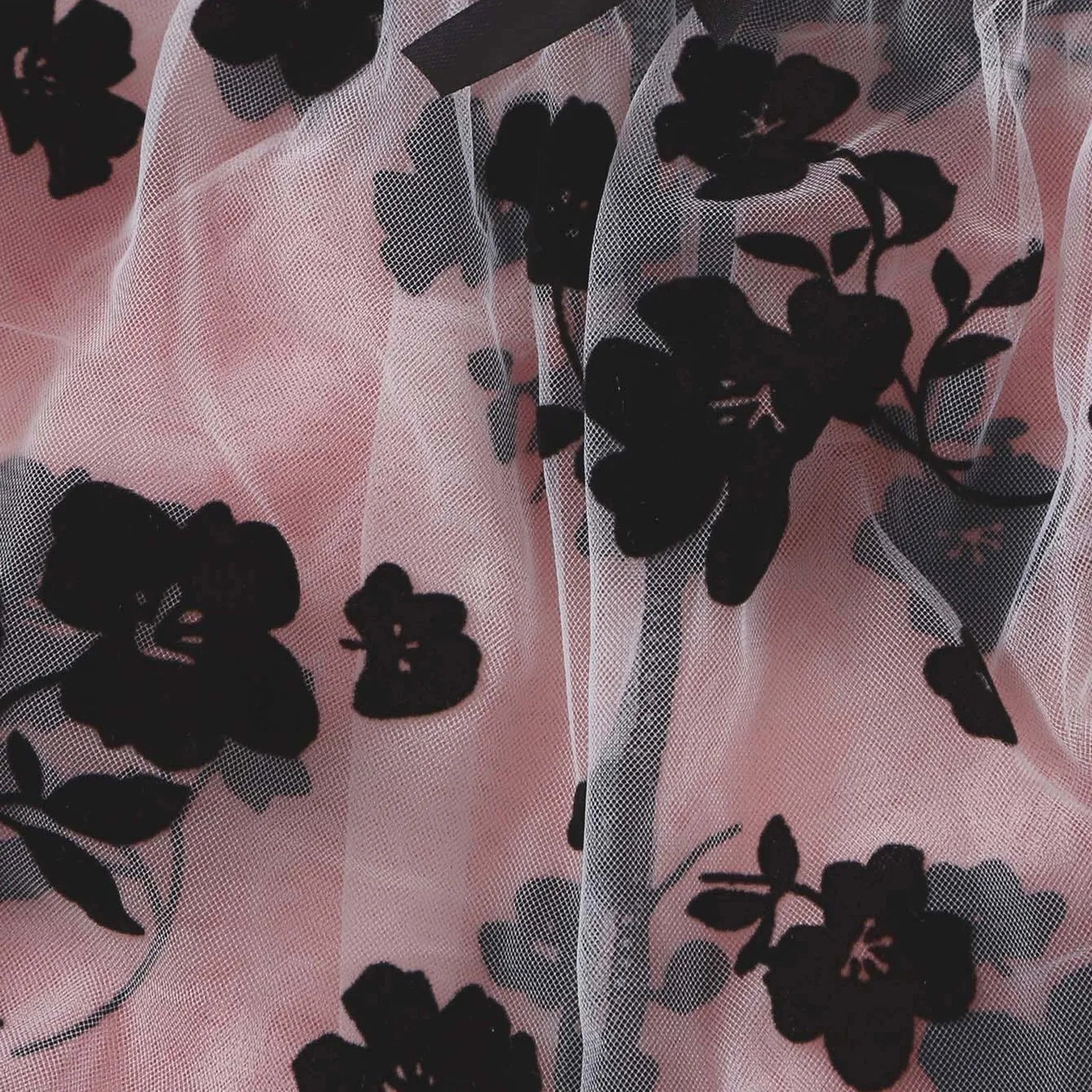 Close-up of black flowers and stems across pale sheer mesh in the lingerie set.