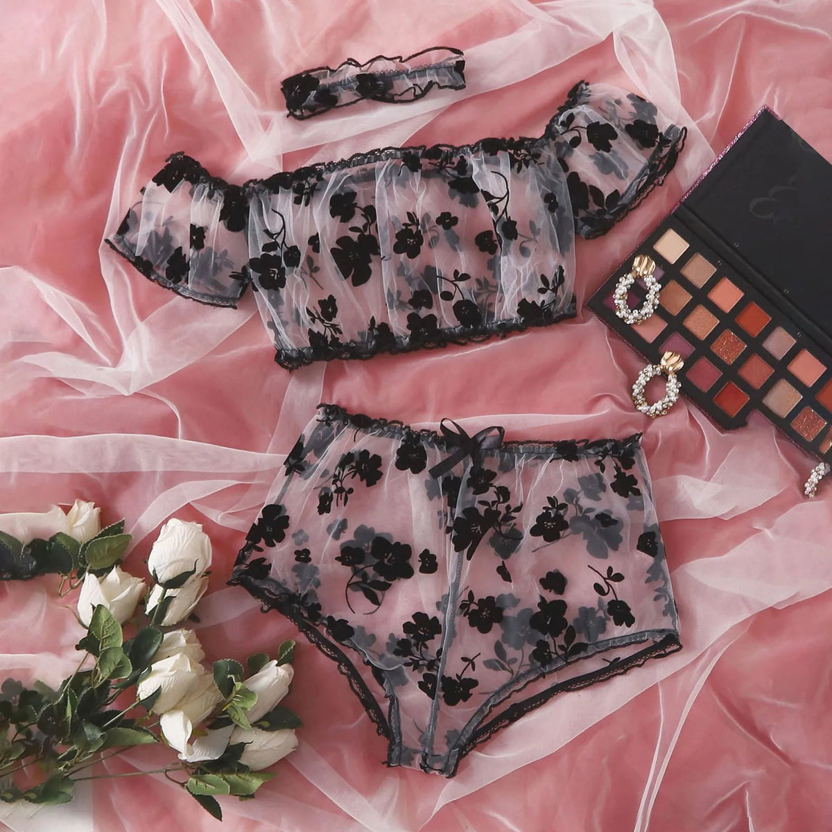 Sheer black floral top, briefs and matching choker arranged on pink satin.
