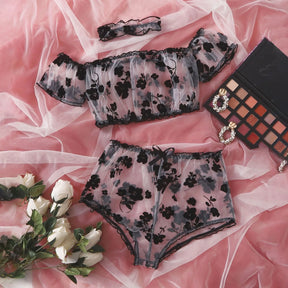 Sheer black floral top, briefs and matching choker arranged on pink satin.