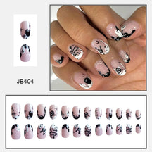Rounded pink false nails with white ghosts, black edge details and small stars, shown worn above a size assortment.