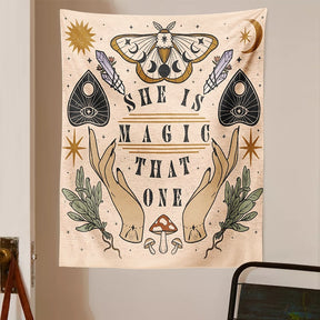 Beige witchy tapestry displayed on a light wall above a chair, with moth wings and moon phases above the printed words.