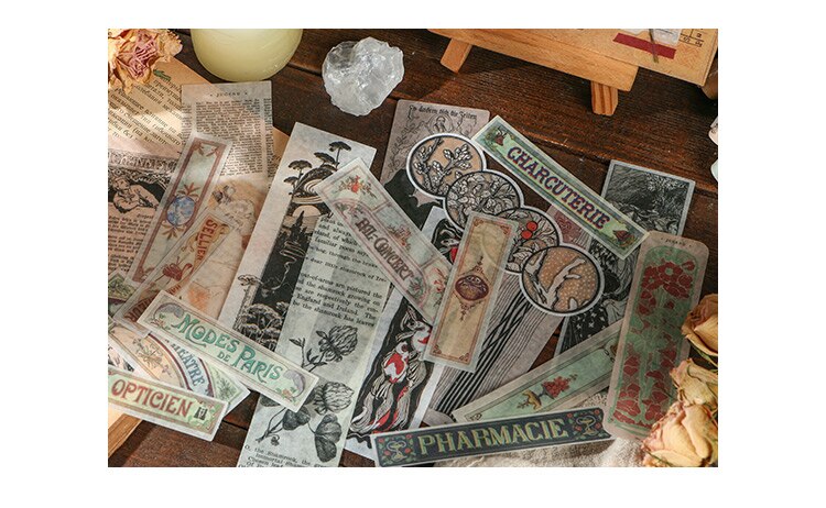 Decorative vintage labels with illustrated flowers, old print and muted coloured borders spread beside a candle.