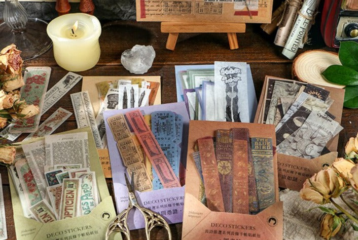 Vintage sticker packs spread across a craft desk beside scissors, dried flowers, books and a candle.