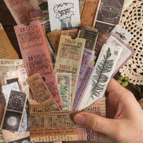 A hand holds a fan of long vintage-style ticket and botanical stickers above a collection of printed strips.