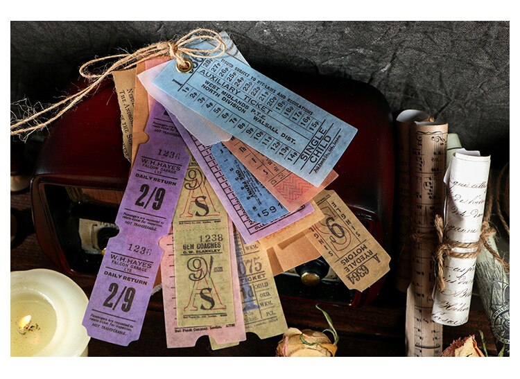 Long ticket-pattern stickers in blue, purple, pink and yellow fanned from a tied paper tag beside a brown book.