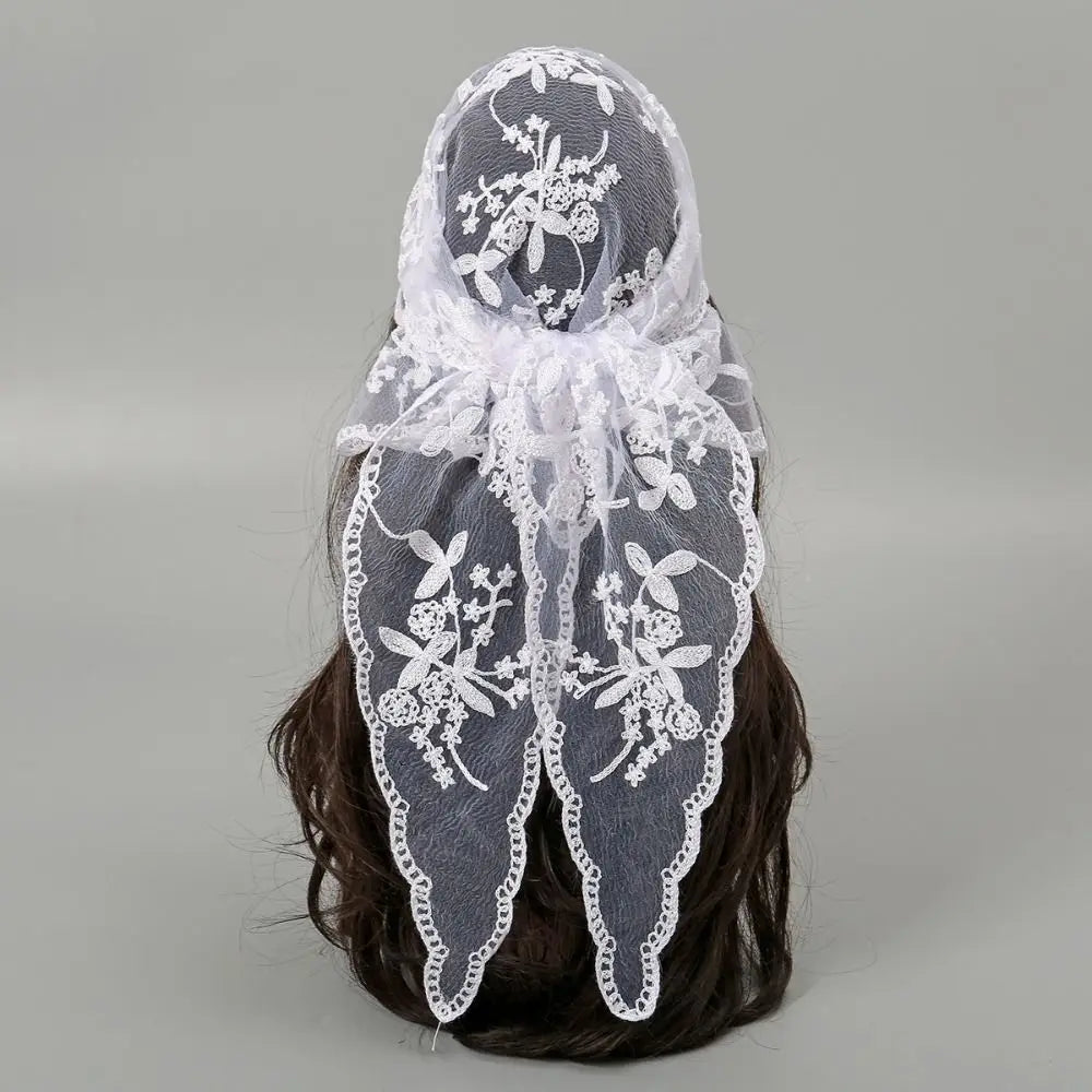 White floral lace triangle headscarf tied in a bow behind dark hair on a grey background. Two tapered ends show the floral pattern, openwork and scalloped borders.