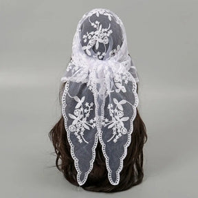 White floral lace triangle headscarf tied in a bow behind dark hair on a grey background. Two tapered ends show the floral pattern, openwork and scalloped borders.