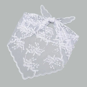 White floral lace bandana tied in a bow and laid flat on a grey background. The triangular floral panel and scalloped edges are visible below the tied ends.