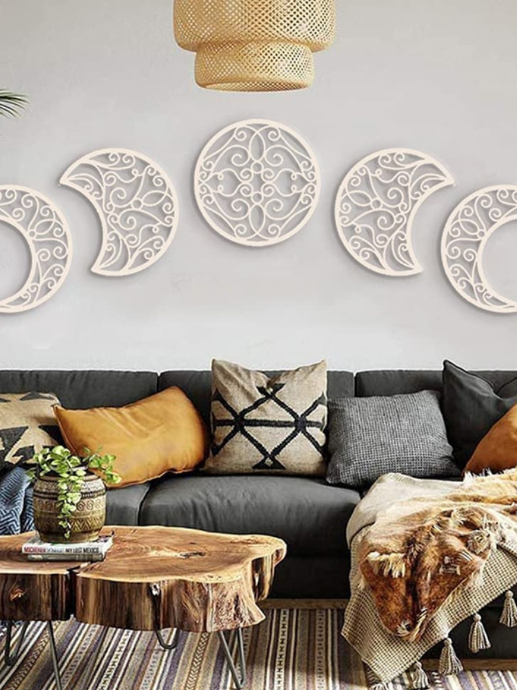 Five white wooden moon-phase cutouts with open scrollwork arranged in an arc above a dark sofa and wooden coffee table.