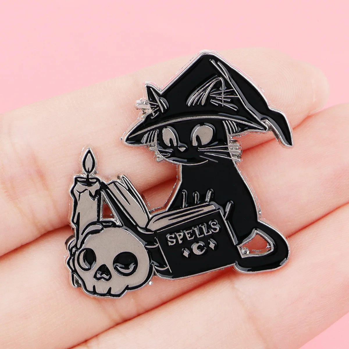 Witch cat spellbook pin resting on a hand to show its scale