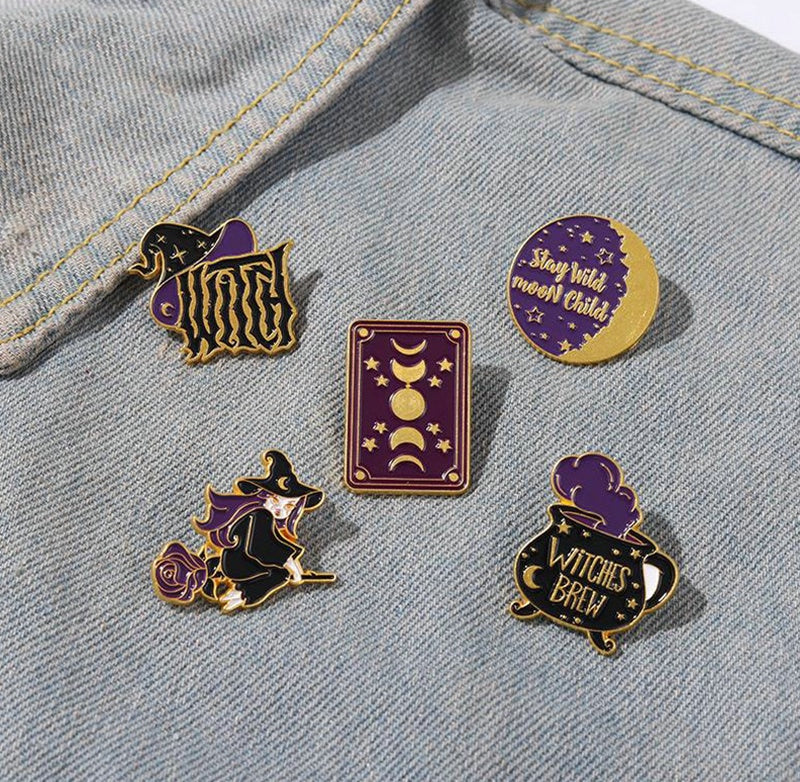 A five-pin witchery cluster on a denim jacket, with the rectangular moon-phase pin centred between the other purple and black designs.