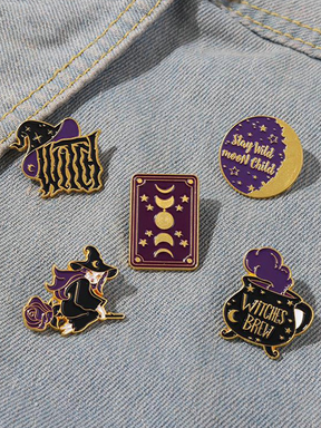 Five purple and black witchy enamel pins arranged on blue denim, with gold-tone outlines around a witch, hat, cauldron and two moon designs.