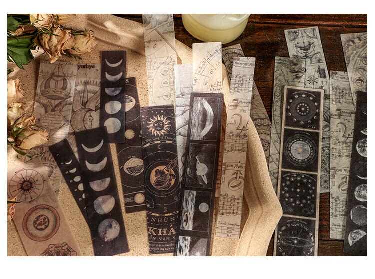 Long celestial sticker strips with moons, orbit diagrams and dark astronomical illustrations spread across a wooden surface.