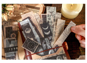 Moon-phase and celestial sticker strips tucked inside a brown journal, with a hand holding one strip beside a candle.
