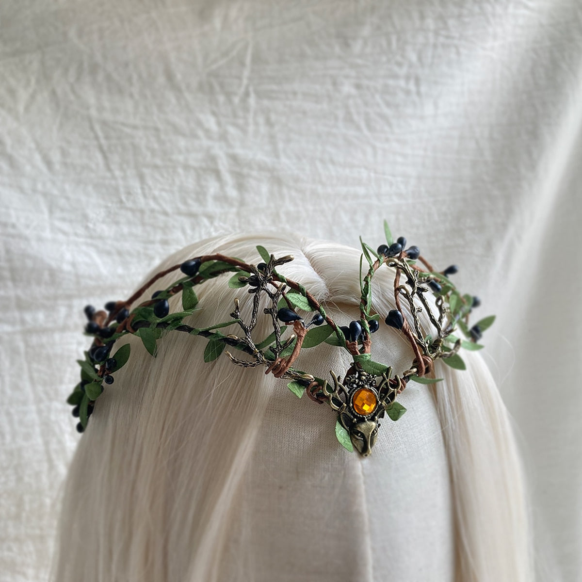 Woodland tiara on pale hair with dark buds, green leaves, branching antlers and an amber-coloured centre.