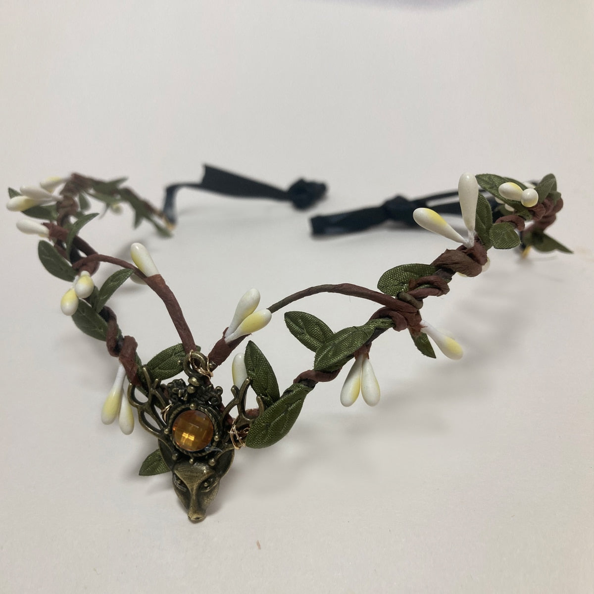 Brown branch-style tiara with white buds and green leaves framing an amber-coloured central accent.