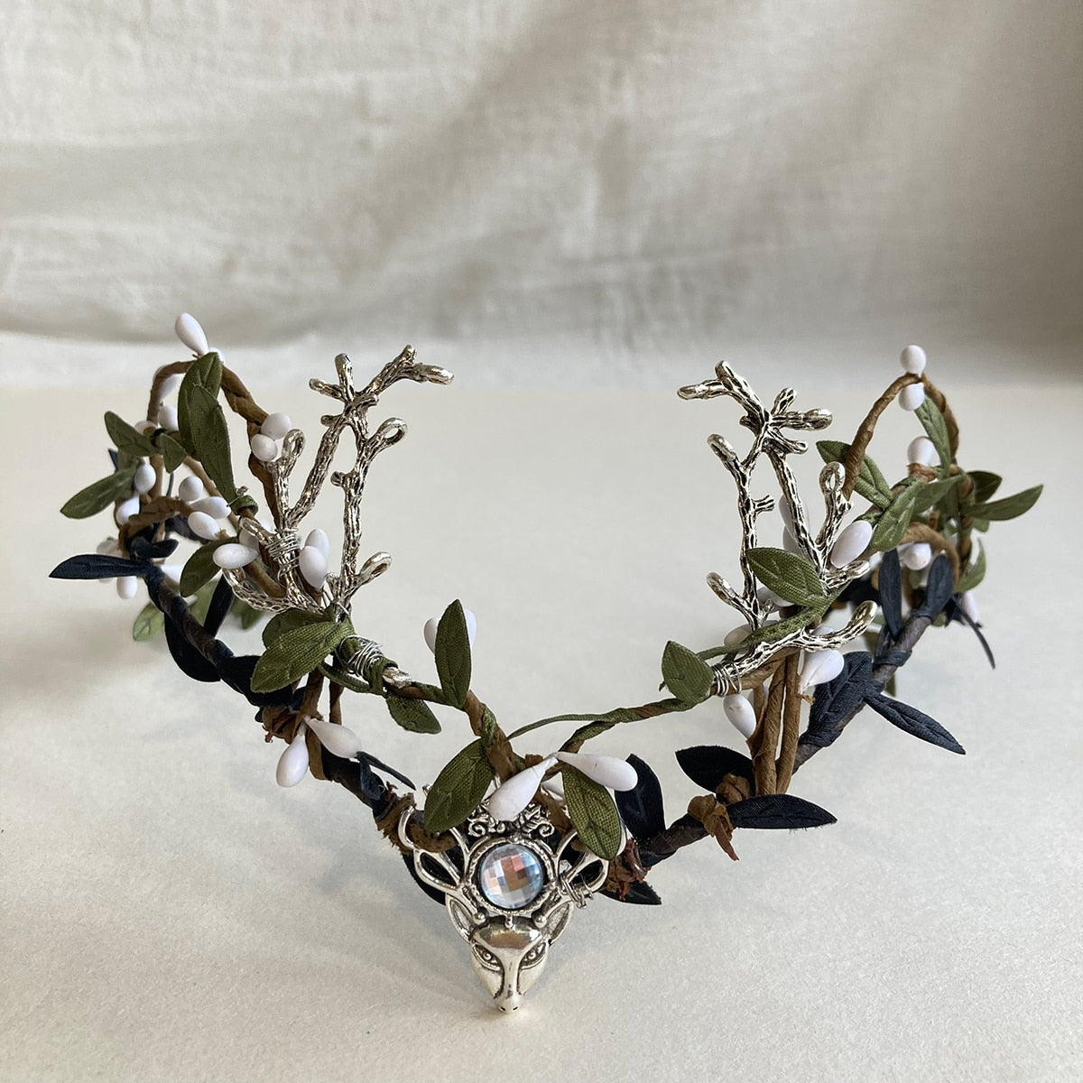 Front view of a silver-tone antler headpiece with clear centre detail, green leaves and contrasting pale and dark buds.
