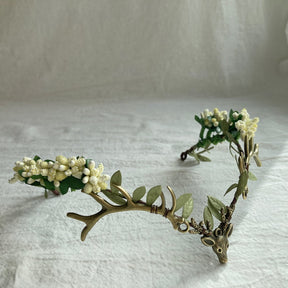 Woodland headpiece with a bronze-tone stag front and clusters of tiny pale buds among green leaves.