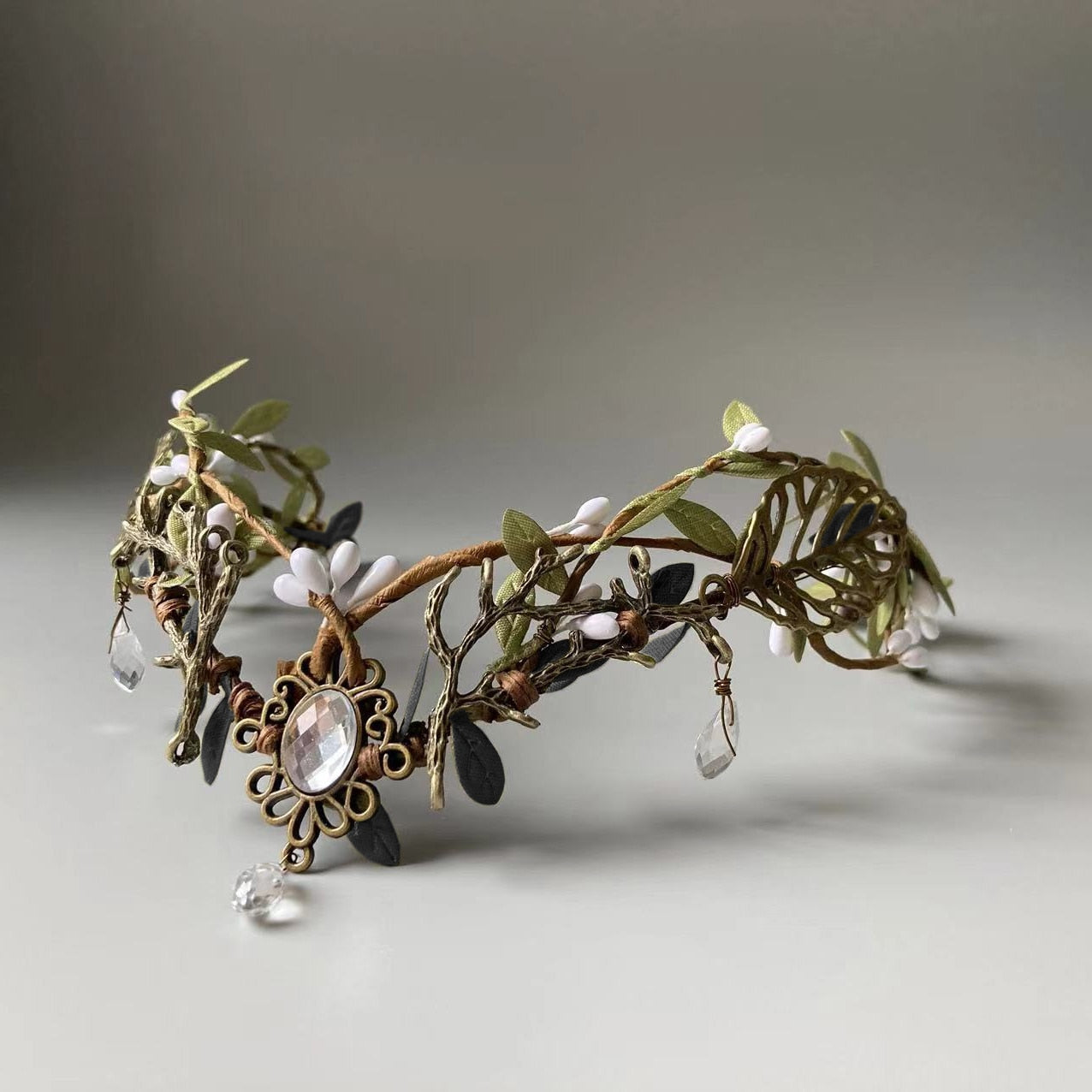 Antiqued gold-tone leafy tiara with pale buds and a clear oval centre ornament ending in a hanging teardrop.