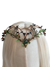 Front view of an elf tiara on pale hair, with bronze-tone antlers, green foliage, dark buds and a green centre jewel-like detail.