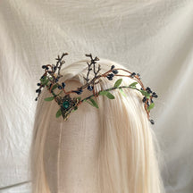 Angled view of the green-centred berry-and-antler tiara on pale hair, showing the height of its branching details.