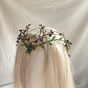 Angled view of the green-centred berry-and-antler tiara on pale hair, showing the height of its branching details.
