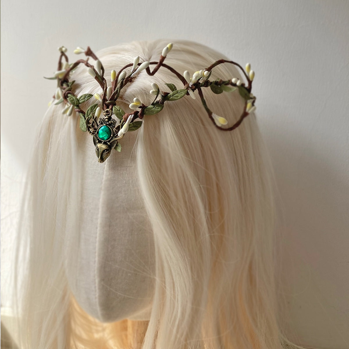 Brown branching tiara with pale buds and leaves frames a green centre accent on a pale-haired mannequin.
